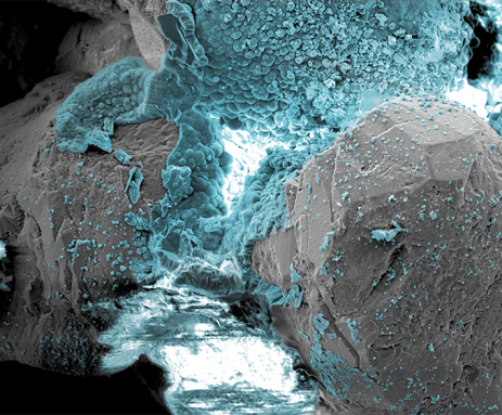 Blue bubbly material fills the middle and top of this microscope image. It shows the minerals created when sand is blasted with low-voltage electricity in an attempt to sand into stone.